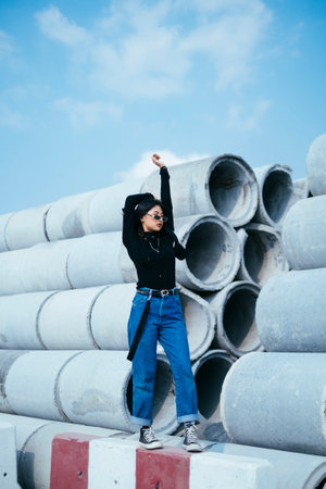 Fashionista girl in black sweater and jeans walk along the big concrete tube's line and stretch her arms.の写真素材