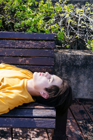 Cropped image of guy in yellow t-shirt and blue pants sleep on the wooden bench in sunlight.の写真素材