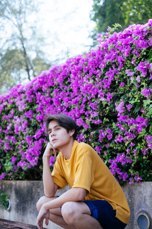 Guy in yellow t-shirt and blue pants sitting next to the pink bougainvillea look at the sky.の写真素材