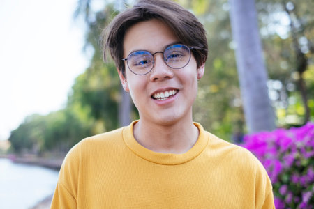 Close up shot of guy in yellow t-shirt and blue pants wearing the eyeglasses in the park and smile.の写真素材