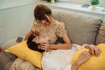 Romantic scene. Asian thai couple at living room. Man laying on woman lap on sofa.