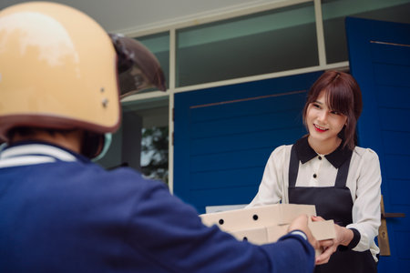 Beautiful asian woman receive box of pizza from delivery man at front door. Pizza boy.