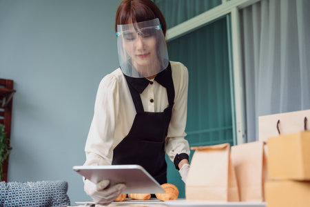 Bakery employee woman checking order on digital laptop for online delivery. Fresh baked croissants.の写真素材