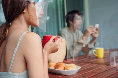 Asian thai couple wearing face shield having brunch at home. Covid-19 outbreak. New normal.の写真素材