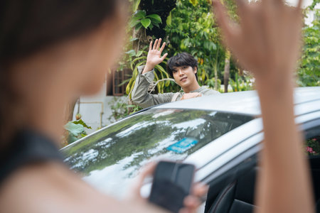 Handsome asian thai man waving hand to say goodbye to his girlfriend before driving a car back home.の写真素材