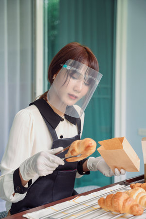 Bakery employee put croissant in paper bag package ready to delivery. Fresh baked.の写真素材