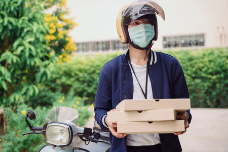 Pizza delivery man wearing mask holding box of pizza outdoors. Covid-19 outbreak.の写真素材