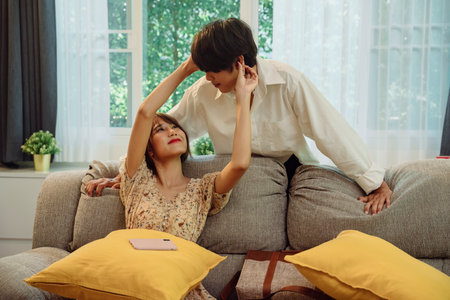 Happy asian thai couple having fun at each other inside living room at a couch.