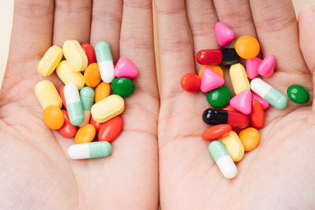 Hands of man holding colourful medicine pills isolate over white yellow background.
