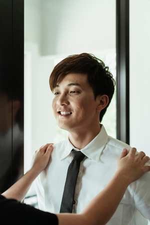 Young asian man on white dress smiling and let his mother dress up for him, adjusting neck tie.の写真素材
