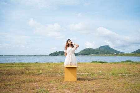 Young asian thai woman hipster curly hairstyle on white dress standing inside the box at lake.の写真素材