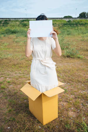 Young asian thai woman hipster curly hairstyle on white dress standing inside the box showing blank paper sign. Copy space.の写真素材
