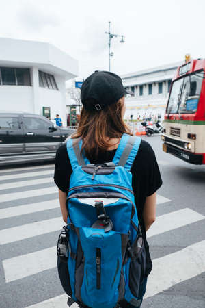 Back view of Backpacker woman in black shirt crossing road in Bangkok.の写真素材