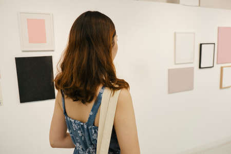 Back view of woman in blue dress watching art frame in gallery.の写真素材