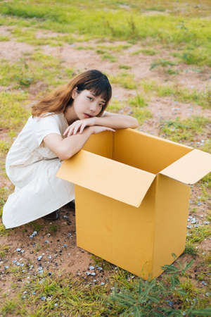 Young asian thai woman hipster curly hairstyle on white dress sitting with opened cardboard box outdoors.の写真素材