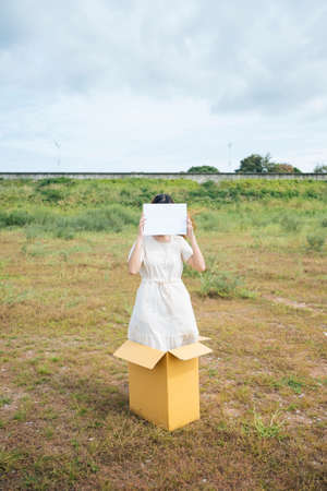 Young asian thai woman hipster curly hairstyle on white dress standing inside the box showing blank paper sign. Copy space.の写真素材