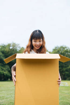 Young asian thai woman hipster curly hairstyle on white dress holding big huge cardboard box. Gift box. Looking inside with surprise expression.の写真素材