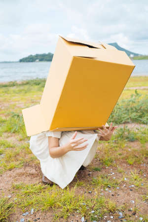 Young asian thai woman hipster curly hairstyle on white dress with cardboard box covering head.の写真素材