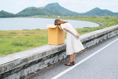 Young asian thai woman hipster curly hairstyle on white dress putting head inside the cardboard box.の写真素材