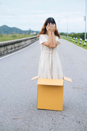 Young asian thai woman hipster curly hairstyle on white dress standing inside the box on the road. Shy woman covering face with hands.の写真素材