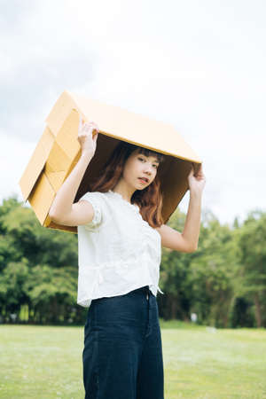Young asian thai woman hipster curly hairstyle on white shirt cover head with cardboard box.の写真素材