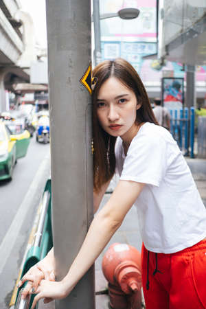 Fashion portrait - Beautiful asian young woman in white shirt and red sport pant hugging the light pole on street. Dirty hugging.の写真素材