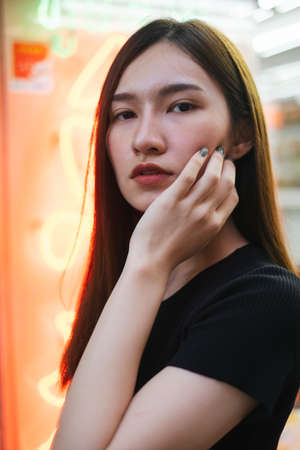 Close up fashion portrait - Beautiful hipster asian young woman in black shirt over neon light background.の写真素材