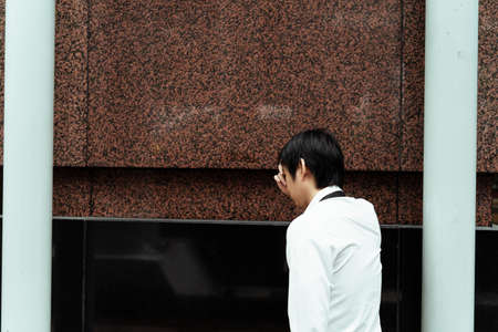 Stressful business man standing next to white pole on the street. Asian business man on white...