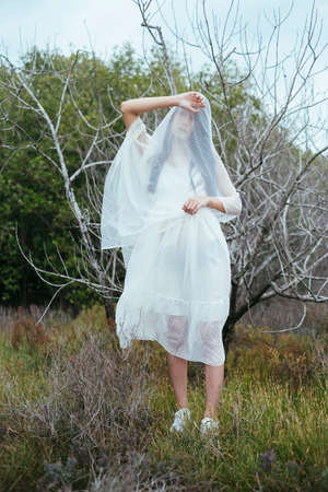 Portrait of young asian long dark hair woman bride cover body with white veil outdoors standing...