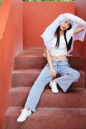 Hipster young asian long dark hair woman bride with white veil sit on stair outdoors. Bangsaen...