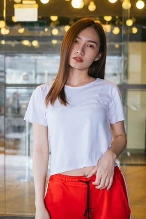 Fashion portrait - Beautiful asian young woman in white shirt and red sport pant posing over beautiful yellow bokeh at background.の写真素材