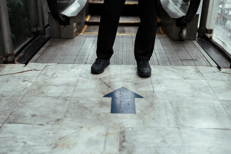 Black arrow poiting at the guy legs in front of escalator.の写真素材