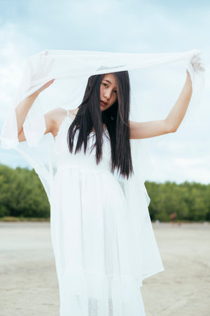 Portrait of young asian long dark hair woman bride with white veil outdoors. Windy day. Country side background.の写真素材