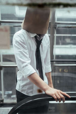 Businessman wearing a paper bag on his head using escalator. Mystery businessman on electric stair.の写真素材