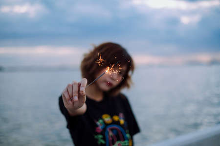 Young asian thai woman short hair in black shirt playing holding with sparkler at the beach in dusk...