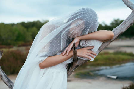 Close up - Portrait of young asian long dark hair woman bride with white veil leaning on dried tree outdoors.の写真素材