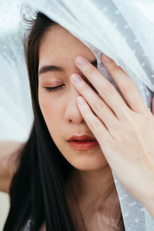 Close up - Portrait of young asian long dark hair woman bride with white veil cover her eye with hand outdoors.の写真素材