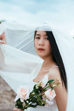 Close up - Portrait of young asian long dark hair woman bride with white veil hold white rose flower outdoors.の写真素材