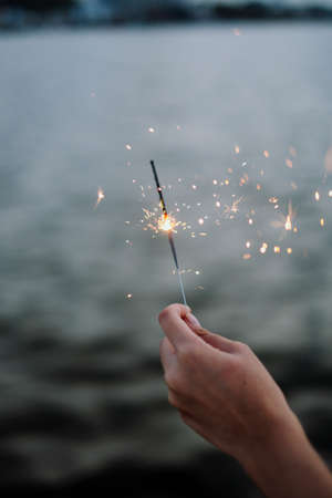 Hand holding a sparkler with blurred deep sea ocean water background at dusk time.の写真素材