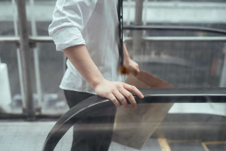Business man hand on escalator handrail and holding paper bag with another hand.