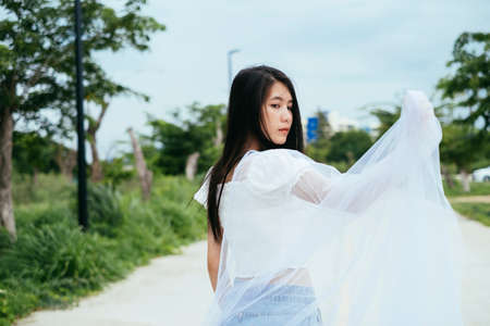 Portrait of young asian long dark hair woman bride with white veil outdoors.