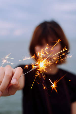 Portrait of young asian short hair woman holding playing with sparkler on the beach.