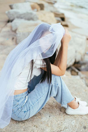 Portrait of young asian long dark hair woman bride with white veil sit outdoors on the beach.の写真素材