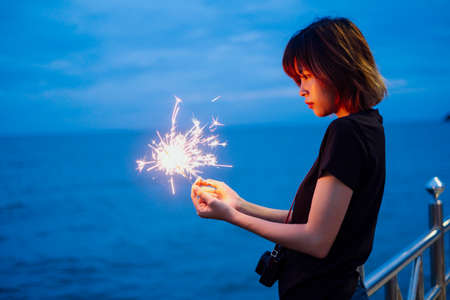 Side view of young asian thai woman short hair in black shirt playing with sparkler at dusk time...
