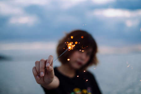 Young asian thai woman short hair in black shirt playing holding with sparkler at the beach in dusk time.の写真素材