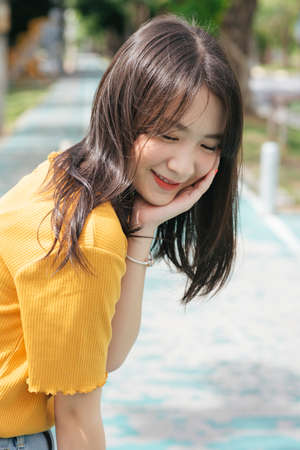 Brunette girl in yellow t-shirt sitting on the little pole at the bicycle lane.の写真素材