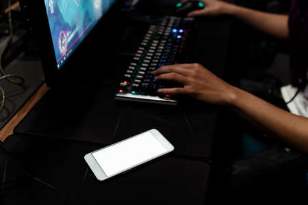 Hands of gamer playing game, typing on keyboard. Empty screen on smartphone putting close to keyboard.の写真素材