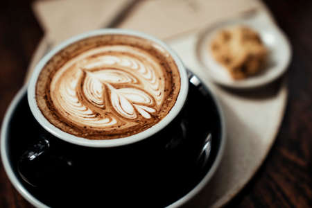 Coffee latte art in a luxury cup serve with a piece of cookie on a plate.の写真素材