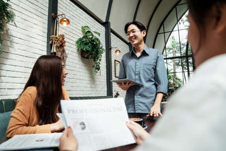Three young asian business people using tablet in the meeting to explain their business concept and idea. The meeting taking place in cafe. Young business boy making presentation to their colleagues.の写真素材