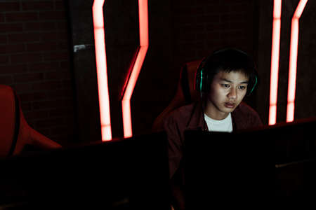 Serious gamer playing game on PC looking at monitor screen in neon red light room.の写真素材